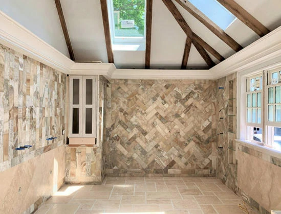 A room under construction with two walls tiled in a chevron pattern, a sky light, and exposed ceiling beams.